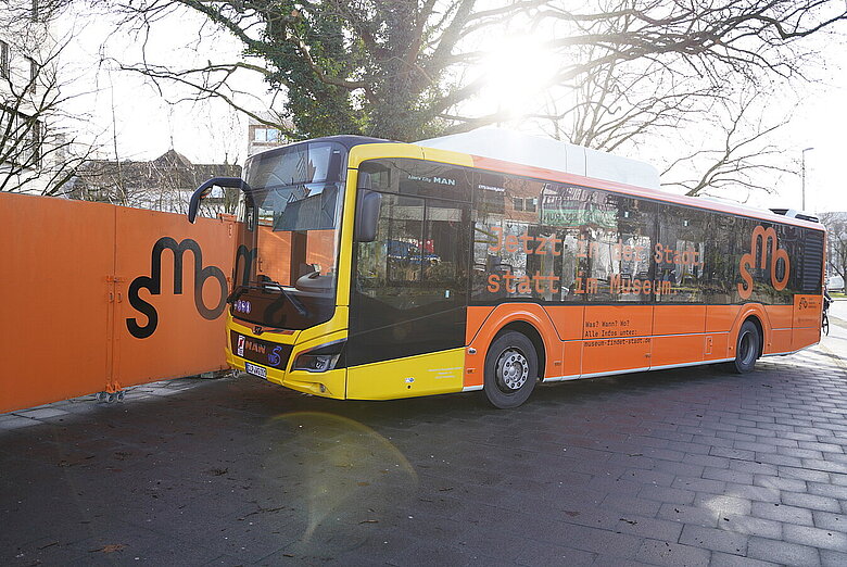 SMO-Bus vor dem Bauzaun des Stadtmuseums